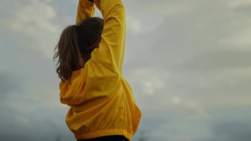 Woman Stretching Arms Upward Against Cloudy Sky Background