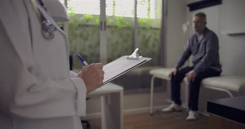 Doctor Taking Notes on Patient in Examination Room