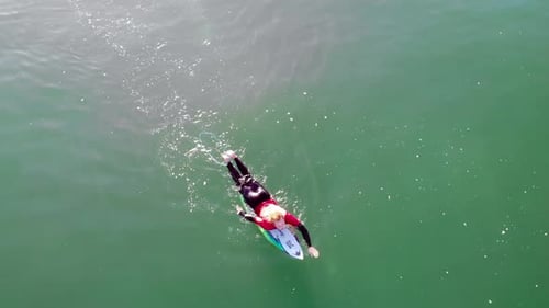 Male surfer Zander Adelsohn in red wetsuit paddles in Pacific Ocean at Huntington Beach, California