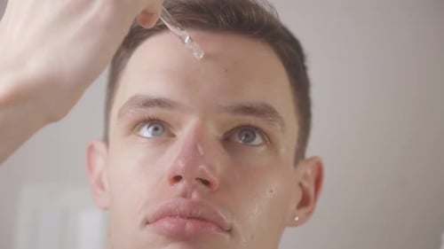 Close Up Of A Man Applying Drops Of Serum On His Face.