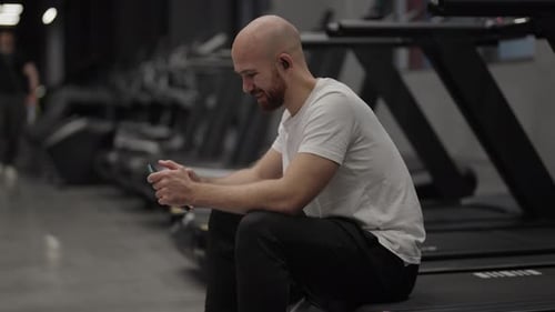Smiling Man Using Smartphone in Gym After Workout on Treadmill