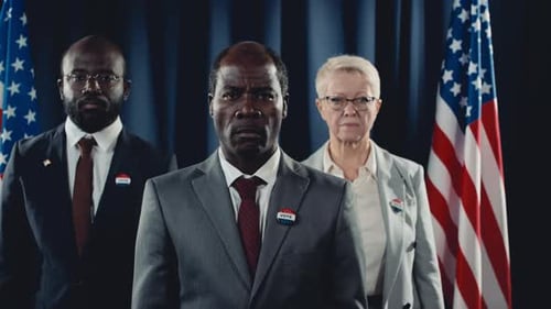 People in Suits stand in front of flags