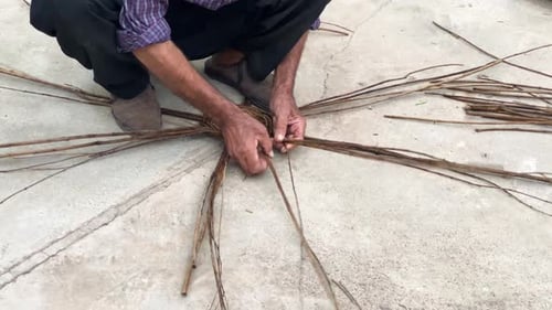 Man weaving together sticks on concrete