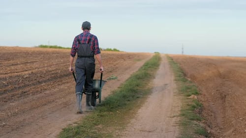 Ein Bauer geht eine Landstraße entlang und schiebt einen Karren vor sich her