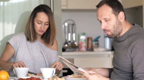 Couple Eating Breakfast and Reading Newspaper Together