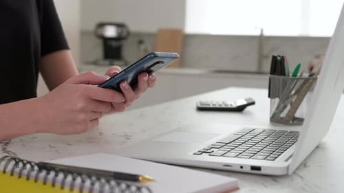 Nahaufnahme einer Frau, die ein Smartphone benutzt, während sie zu Hause am Tisch in der Küche sitzt