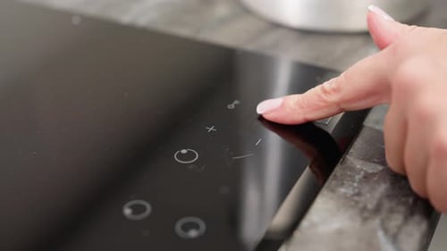 Finger Touches Power Button on Induction Cooktop