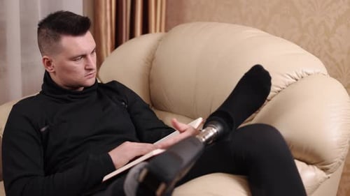 Man with prosthetic leg relaxing and reading book