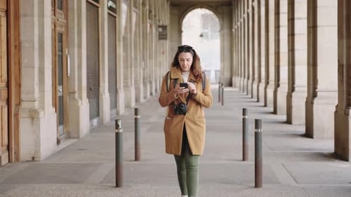 Woman Using Mobile Phone While Walking Through Archway