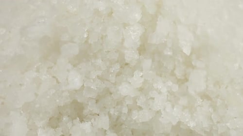 Large crystals of natural sea salt fall onto a wooden surface. A big pile of salt, lots of salt.