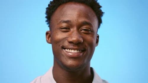Junger Afroamerikaner posiert vor blauem Hintergrund und zeigt Daumen hoch