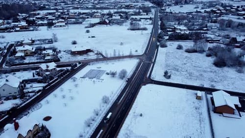 Aerial fly slow over car driving through winter snow covered village at dusk, lonely town