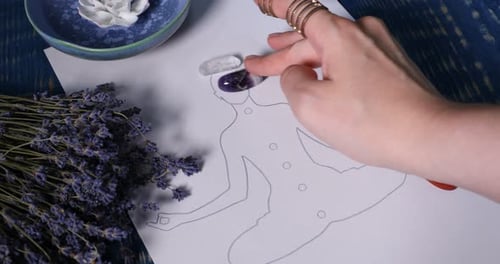 Mujer colocando piedras preciosas en el dibujo de un humano con chakras en una mesa de madera azul, primer plano