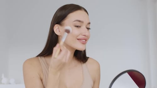 Woman Applies Makeup with Brush Looking in Mirror