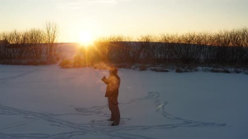 Person stand on frozen lake during winter sunset and exhale cigarette smoke