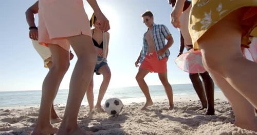 Diverse friends play soccer on a sunny beach