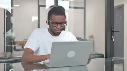 Young African Man with Headset in Call Center Working on Laptop