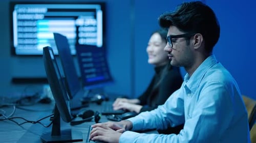 Male and female tech support or data analysts typing on keyboards with multiple screens showing data