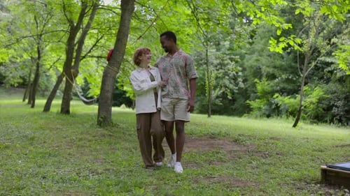 Young multiracial couple is holding hands and talking while enjoying a walk together in a green park