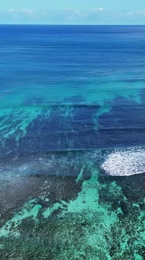 Aerial drone view capturing waves breaking along a coral reef with vibrant turquoise lagoon waters,