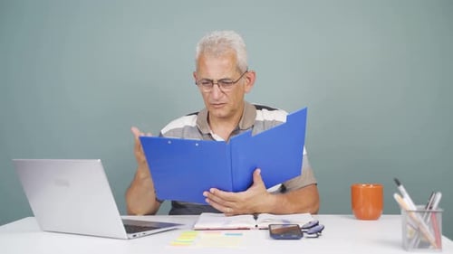 Man working on laptop throws files angrily.