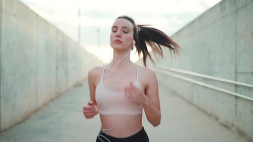 Young woman in wired headphones, runs along the pedestrian crossing to the beach