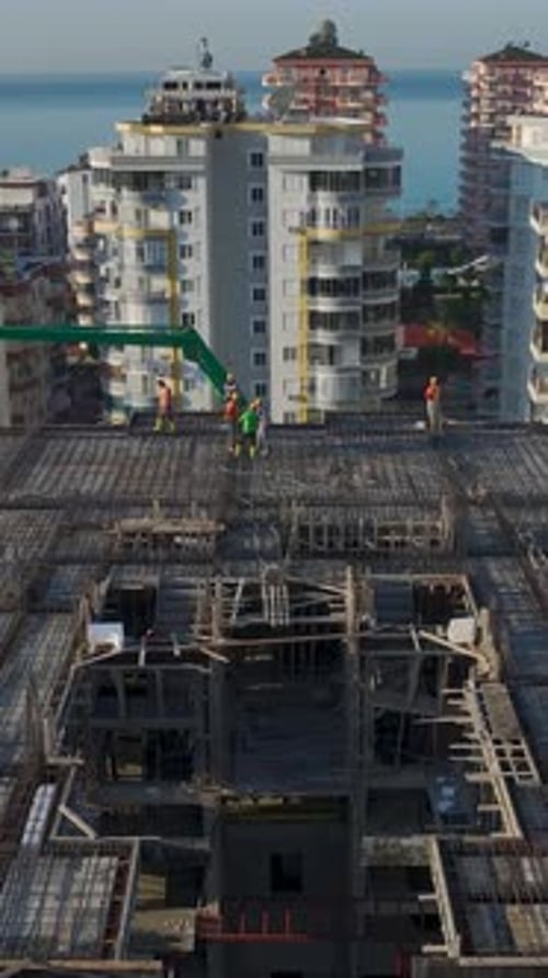 Vertical Video of Engineers Reviewing Plans While Workers Pour Concrete and a Crane Assists on Site