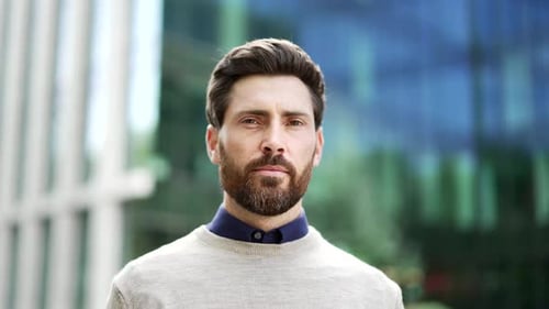 Portrait of serious businessman with beard standing outside city office building. Male professional