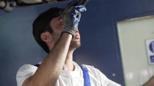 Asian repairman using flashlight inspecting vehicle broken part and repairing car