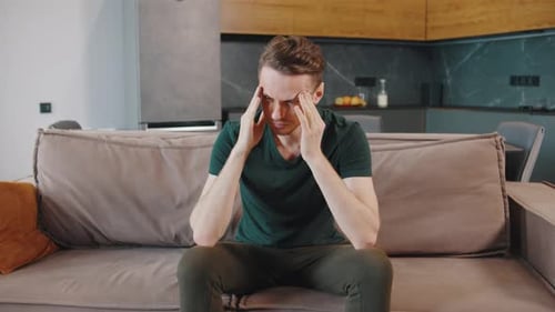 Stressed Man Sitting on Couch Holding Head Possibly Due to Headache or Anxiety