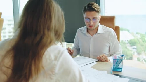 Two Professionals Engage in Discussion at a Modern Office Overlooking a Cityscape Focusing on Their