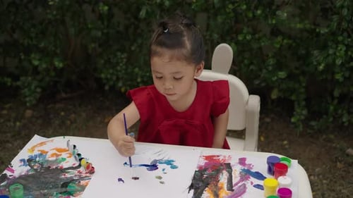 happy toddler girl painting watercolor in a paper at backyard