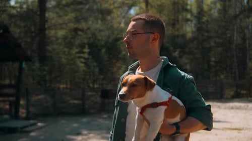 Handsome man with dog in arms walks in forest in summer