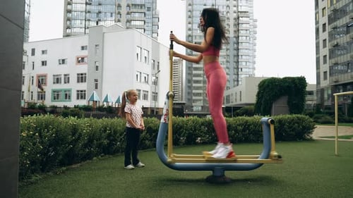 Woman Exercises Outdoors While Child Plays Nearby in Urban Park Setting