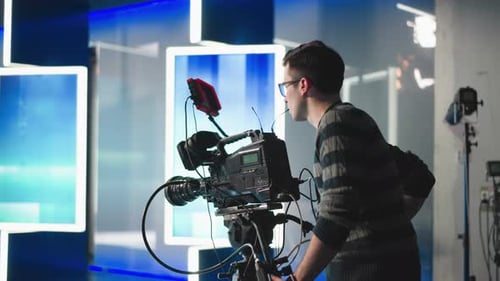 Camera Operator Adjusting Professional Video Camera in Studio with Hightech Lighting Setup