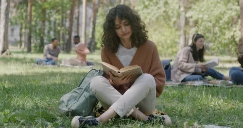 Porträt einer schönen jungen Studentin, die ein Buch liest und sich auf die Prüfung im Park vorbereitet