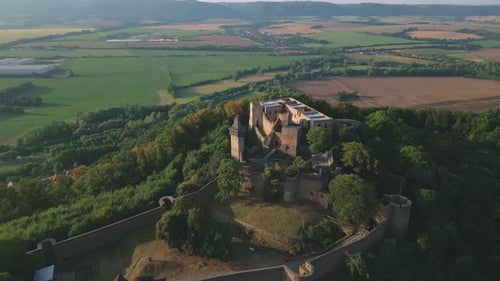 Drone flying over of a large Helfstyn castle with fortified walls surrounded by lush greenery and fi