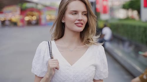 A Happy Woman in a White Dress Strolling Down the Street Smiling