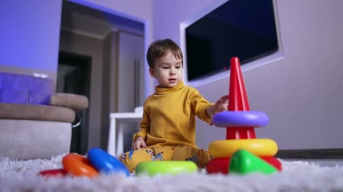 Joli petit garçon calme jouant avec une pyramide. L'enfant est assis sur le sol en train d'assembler un jouet. Vue à angle réduit.