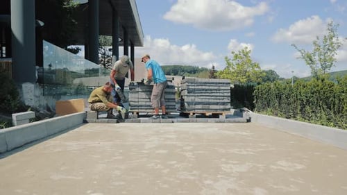Men Laying Pavers Outside Modern Building on Sunny Day