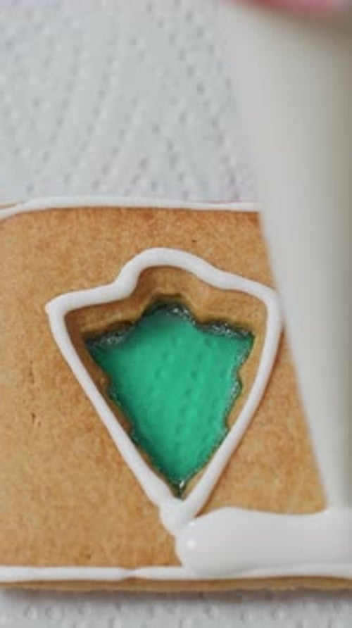 Closeup of Person Icing Cookie with White Frosting and Green Filling Decoration