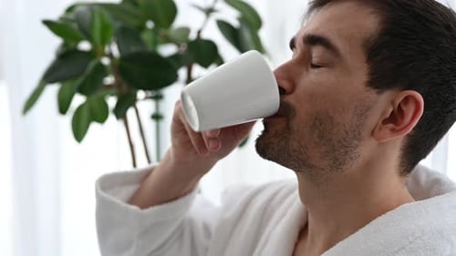 Young Man Drinking Coffee in Robe at Home