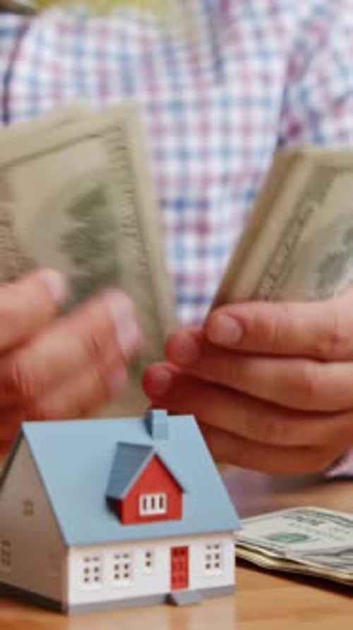 Man Counts Money with House Model on Table