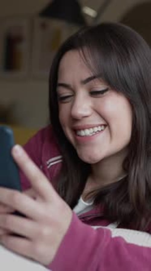 Pretty Young Adult Woman Using Mobile Phone While Relaxing on Sofa at Home