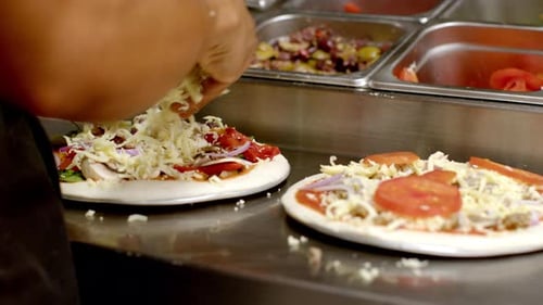 Nahaufnahme eines Kochs, der Käse hinzufügt, um die Pizzen fertig zu machen