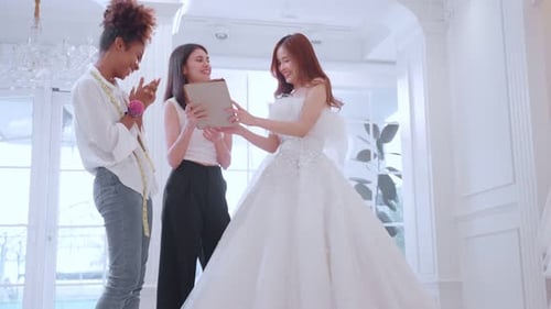 Asian LGBTQ bride trying on wedding gown with her fiance in studio.