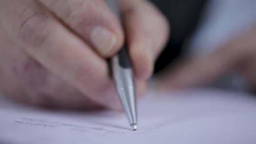 Close-up of a person writing on paper, focus on hand and pen, blurred background