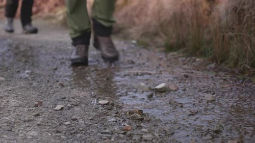 Close up of two mens feet hiking on a wet trail wearing hiking boots and stepping through water and
