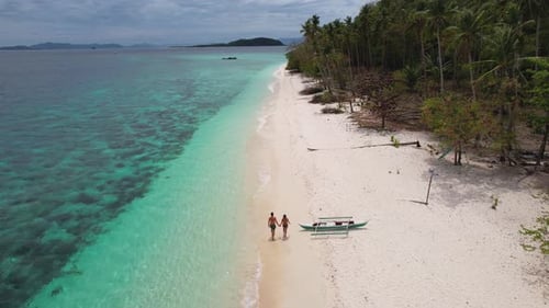 4K drone video of a couple walking hand in hand along a white sand beach on a tropical island in Pal