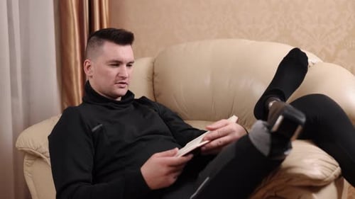 Man Reading Book on Couch Indoors
